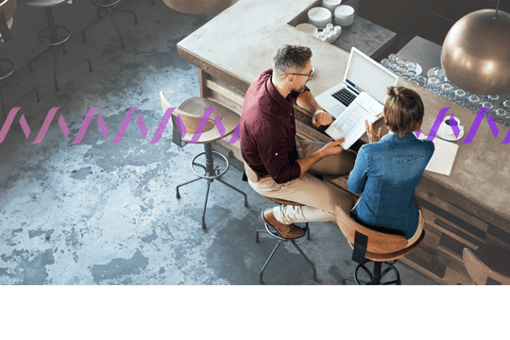 Vonage around the world Image of two workers sitting on stools at a counter with a laptop, reviewing paperwork
