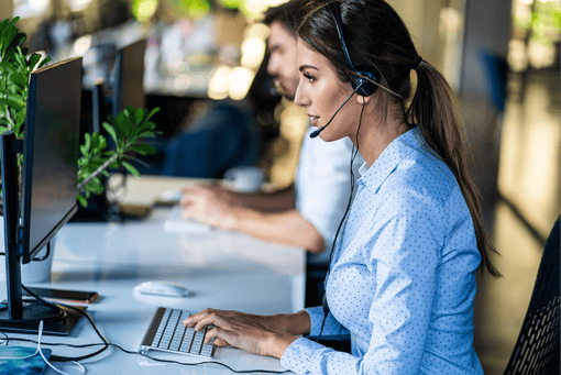 UC Call Center Software Guide Article Header Photo of woman working in a call center. She is typing on her computer keyboard while talking to a customer over her headset.