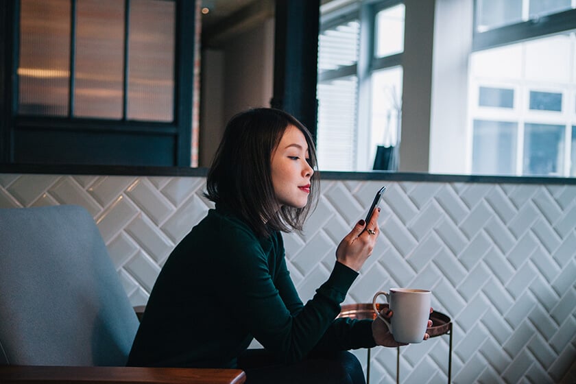 woman looking at mobile device  and holding coffee cup