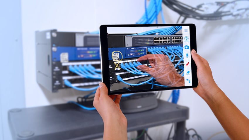 hands holding up a tablet to show a remote help agent the back of a computer network